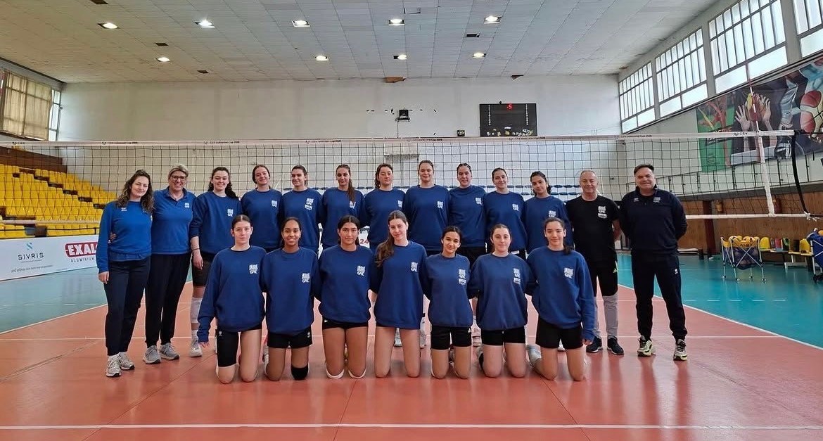 Womens volleyball team posed in front of volleyball net.